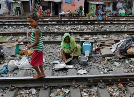 Seorang anak laki-laki meeniti rel melewati seorang wanita yang membersihkan peralatan dapurnya di antara rel kereta api di daerah kumuh Kalkuta, India. (Foto:Reuters/Al Jazeera)