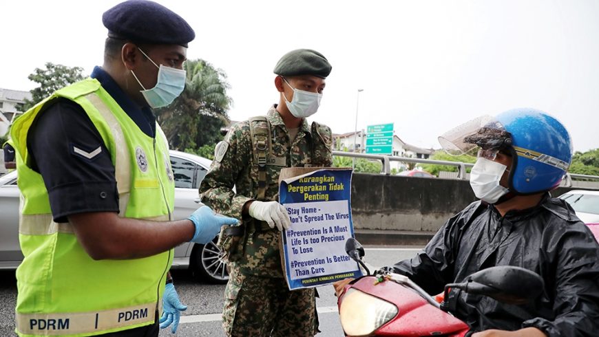 Seorang tentara dan seorang polisi menunjukkan plakat pembertahuan kepada pengendara sepeda motor di sebuah pos yang didirikan untuk menegakkan perintah gerakan kontrol di Kuala Lumpur, Malaysia. (Foto: Reuters/Al Jazeera)