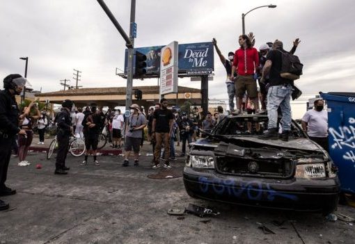 Para pengunjuk rasa berdiri di atas sebuah mobil polisi yang telah terbakar di Los Angeles, California.(Foto: EPA/BBC News)