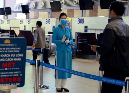 Seorang staf maskapai penerbangan menginstruksikan kepada penumpang bagaimana cara check in di bandara Hanoi, Vietnam, sambil menjaga jarak sosial. (Fot: AP/Al Jazeera)