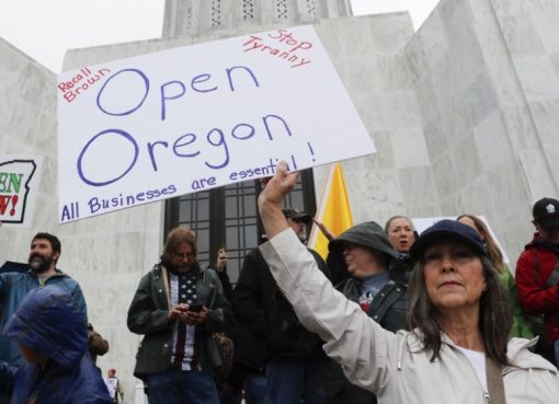 Seorang wanita memegang pamflet bertuliskan Open Oregon di tangga ibukota negara bagian di kota Salem Oregon, pada 2 Mei 2020.( Foto: Getty Images/AFP/Al Jazeera)